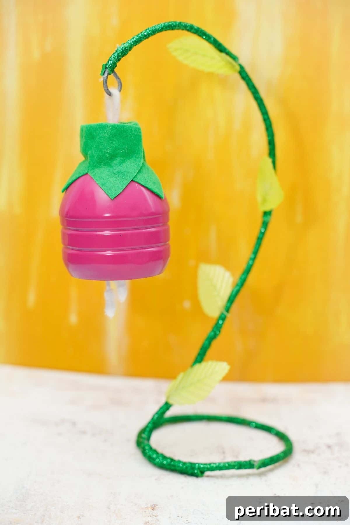 Upcycled Plastic Bottle Blossoms 4 Pink hanging plastic bottle flower with green wire stem on a yellow background