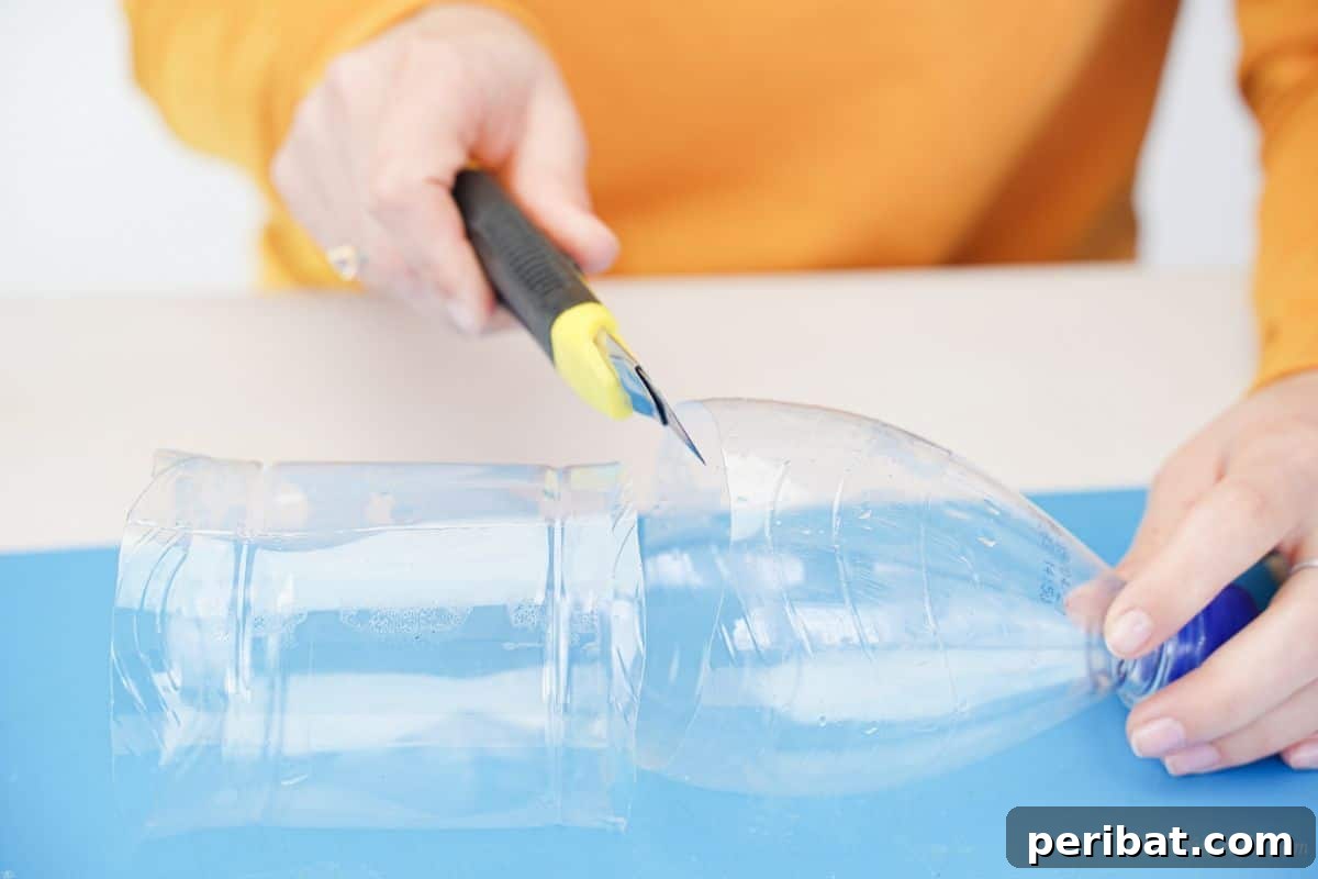 Yellow craft knife cutting the bottom third of a plastic bottle on a blue mat.