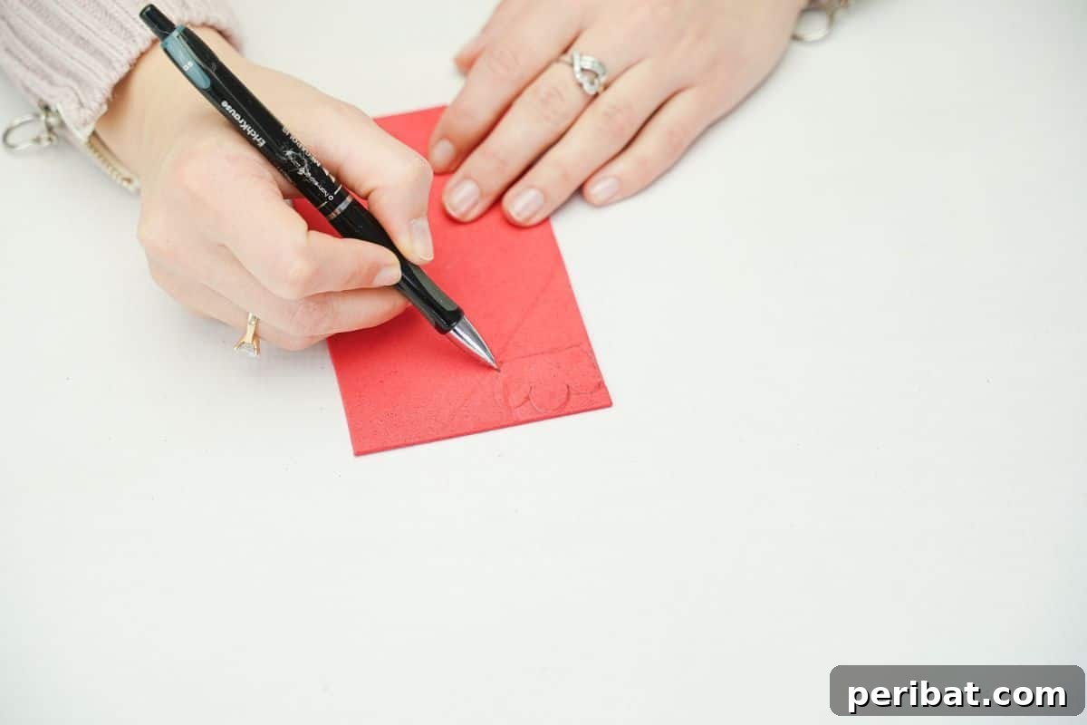 A hand holding a black pen tracing a shape onto red foam paper.
