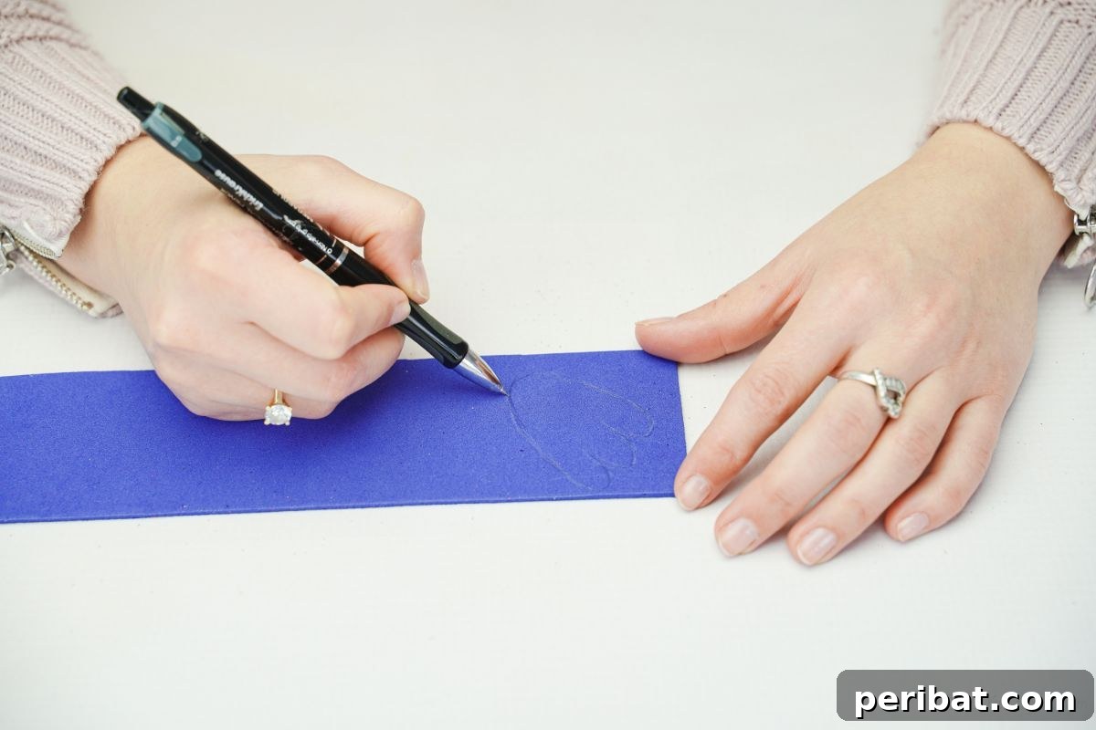 A hand drawing a foot shape onto blue foam paper on a white table.