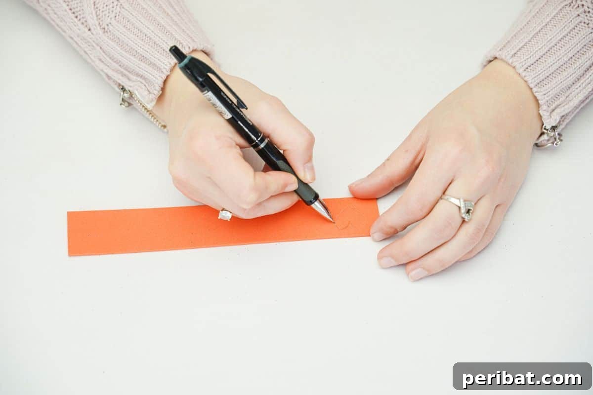 A hand using a black pen to draw on orange foam paper.