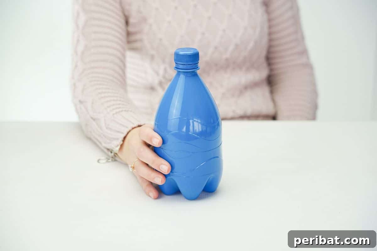 Hand holding a blue spray-painted plastic bottle turkey body on a white table.
