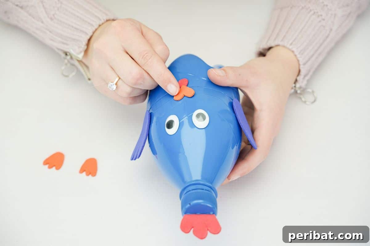 A hand adding a foam beak to the plastic bottle bird's face with hot glue.