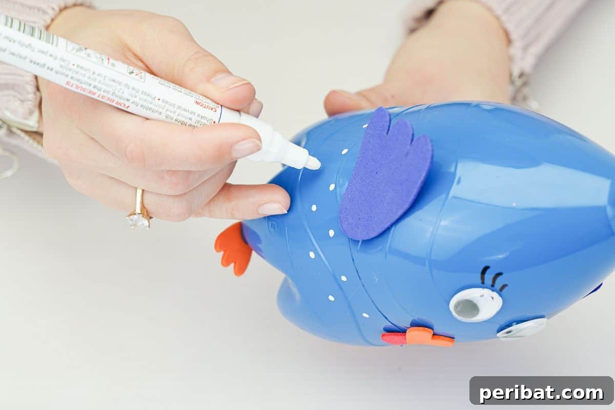 A hand using a white paint pen to make decorative dots on the blue turkey craft.