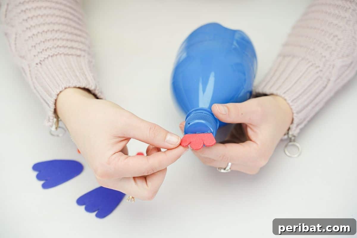 Adding the red wattle to the top of the plastic bottle turkey craft with hot glue.