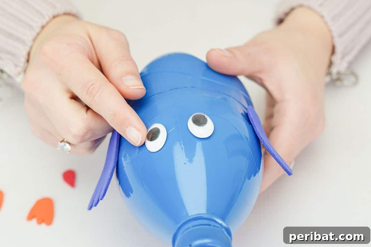 Googly eyes being added to the front of the plastic bottle bird with hot glue.