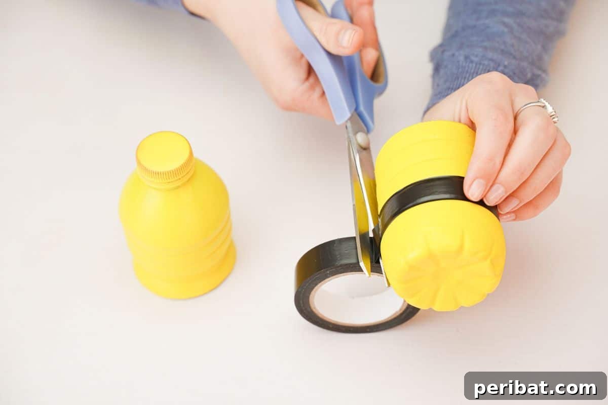 Blue scissors cutting black tape on the edge of a yellow bottle base.