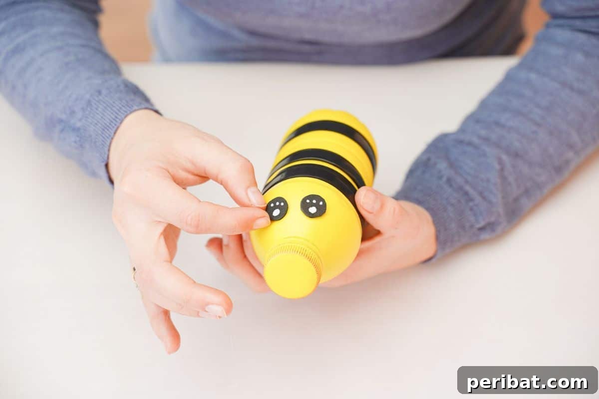 A hand holding a felt eye, applying it to the top of the bee bottle.