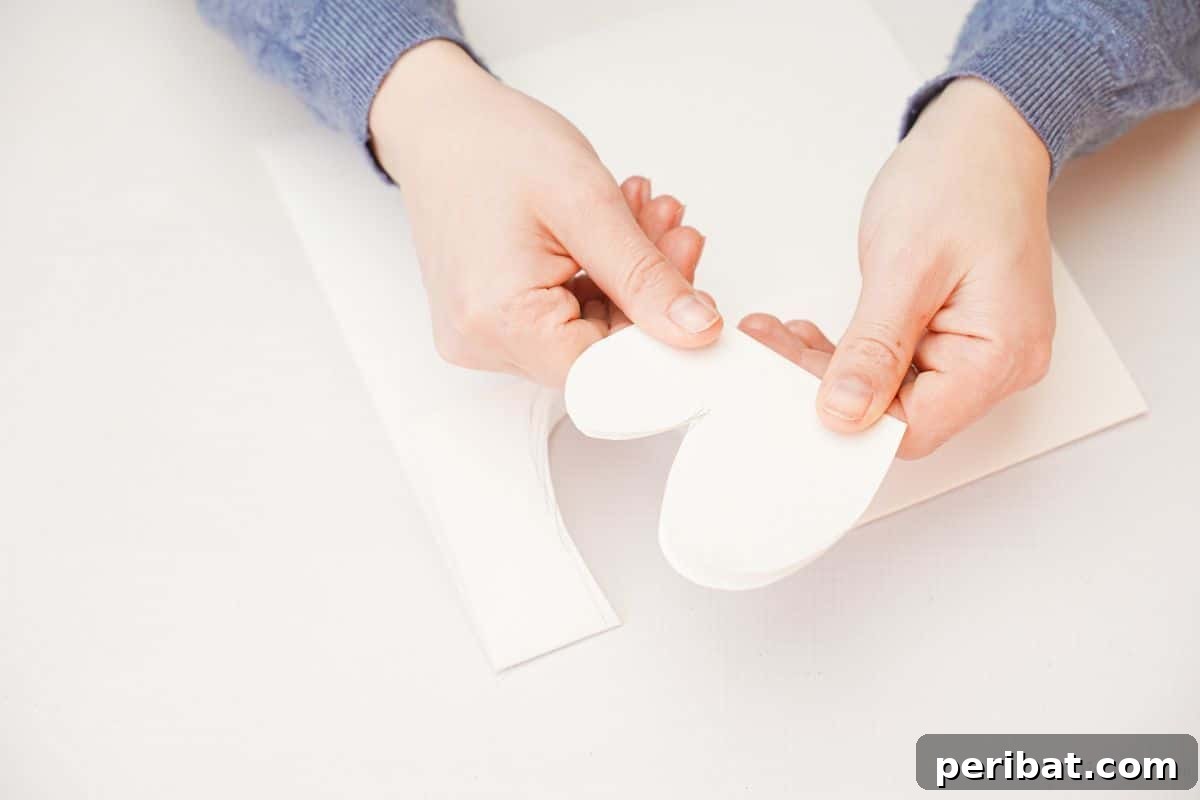 A hand holding a folded, curved piece of white paper, cut into a wing shape.