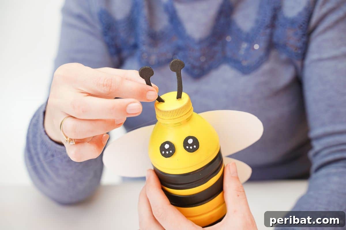 A hand holding a black foam antenna, gluing it to the top lid of the bee bank.