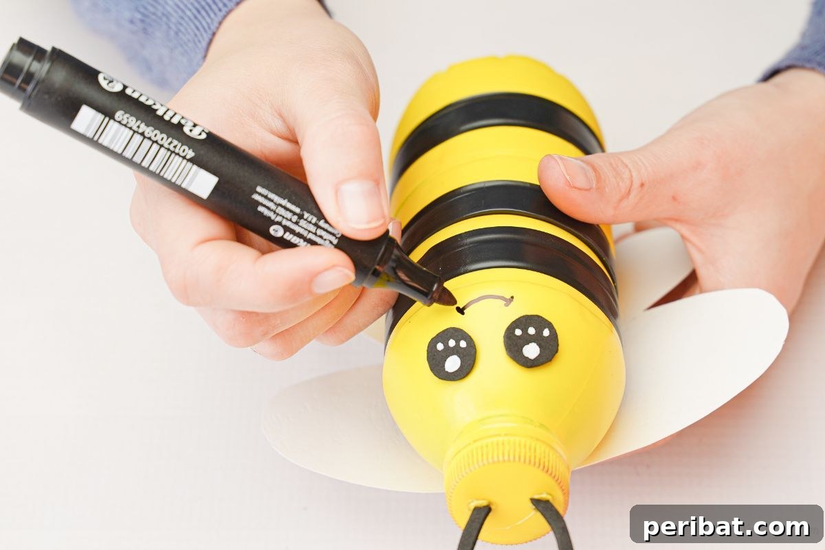 A hand holding a marker, drawing a mouth on the bumblebee bottle.