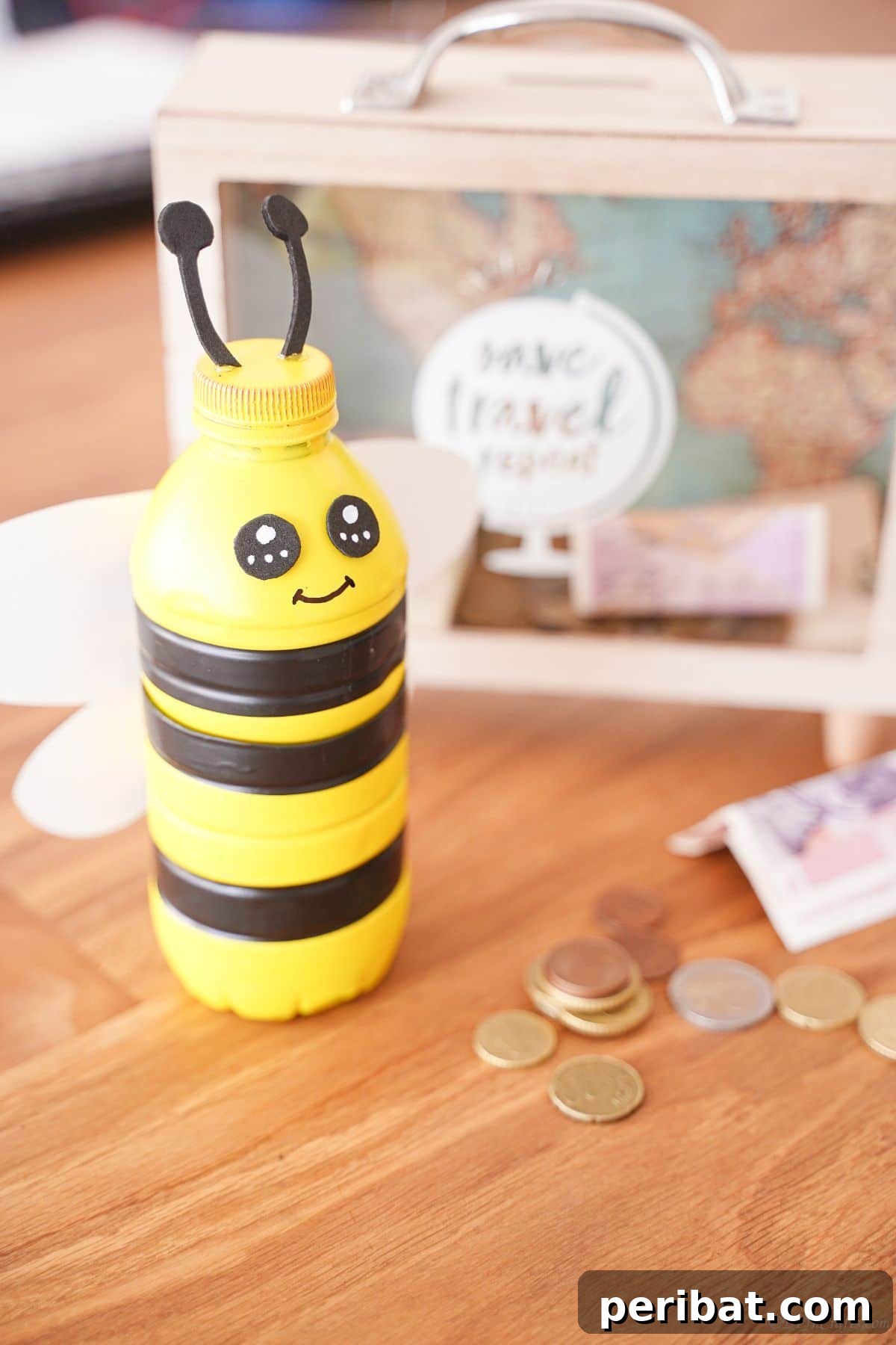 The finished plastic bottle bumblebee bank sitting on a wooden table next to a ticket shadowbox.