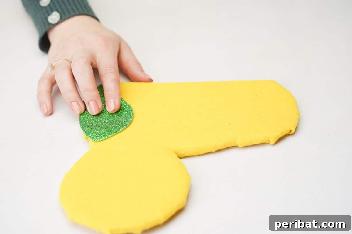 Green glitter foam paper being held on the edge of the yellow caterpillar body