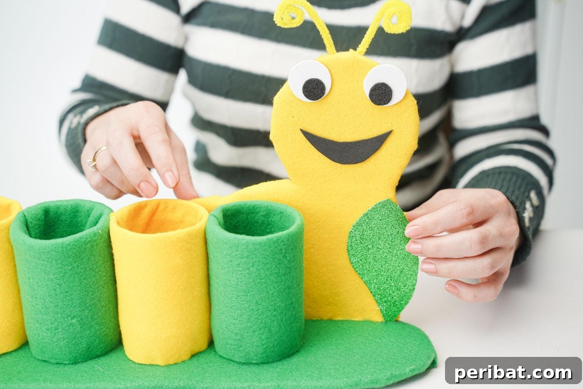 Hands gluing the caterpillar body to the cardboard strip behind the bottles