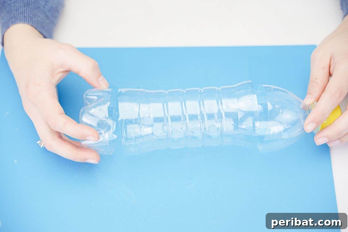 Hand holding the bottom of a plastic bottle after being cut on a blue mat, showing the flat edge.