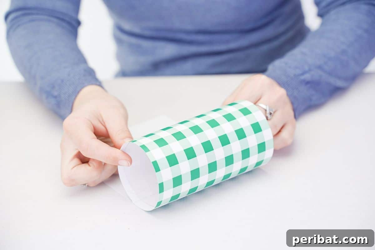 Hand holding a clear plastic bottle section wrapped with green and white checked scrapbook paper.