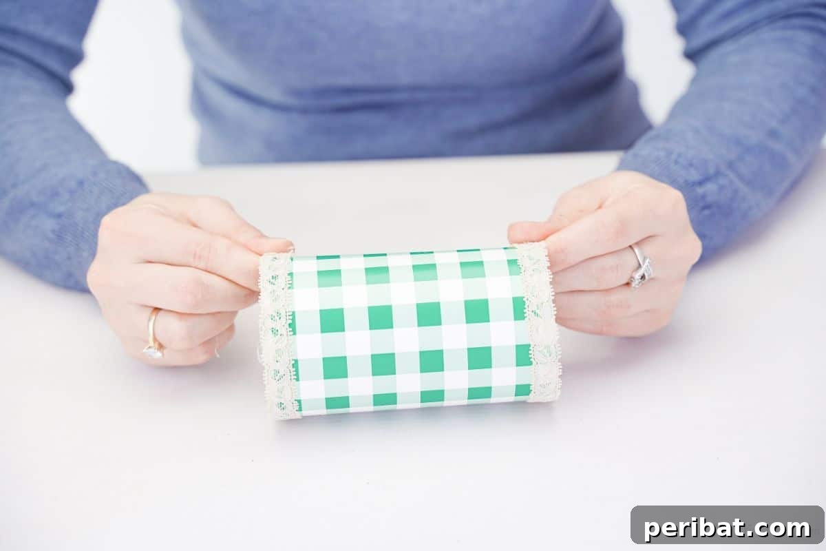 Lace being held and glued onto the ends of a green and white checked covered bottle, showing the trim detail.