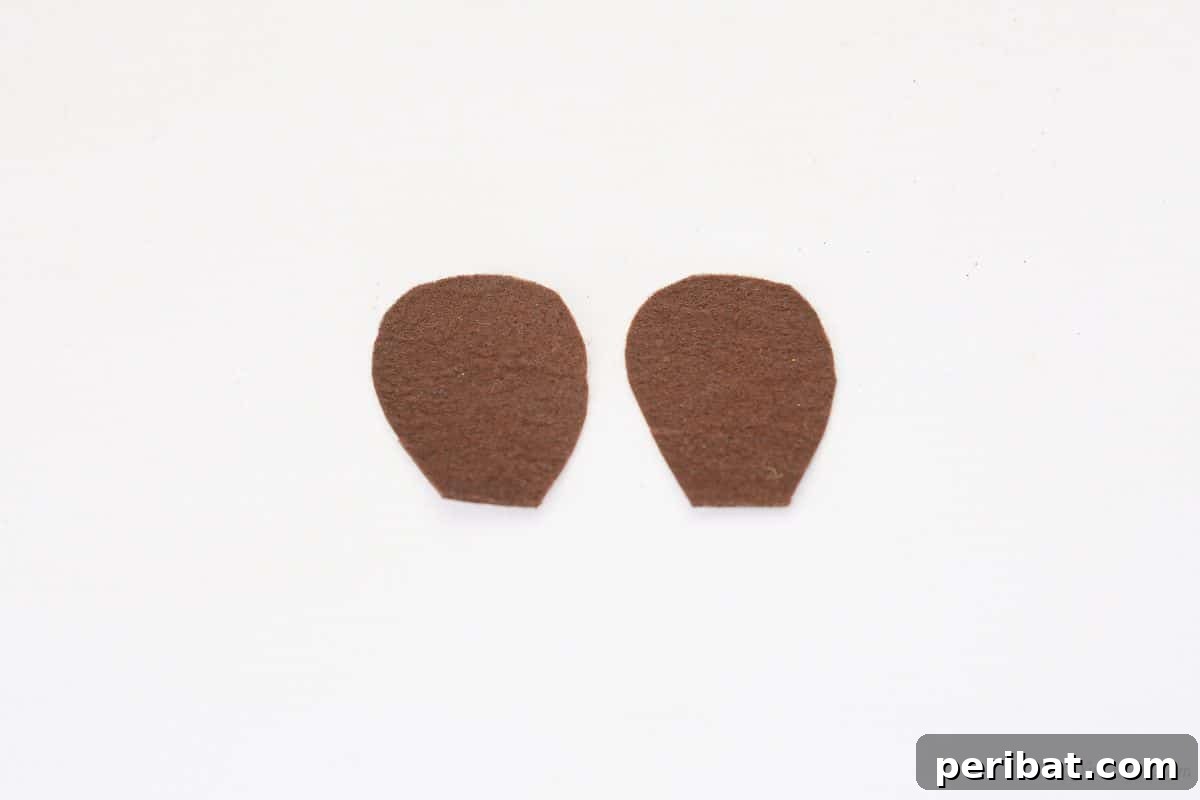 Two oval brown felt ear pieces neatly cut and placed on a white crafting table.
