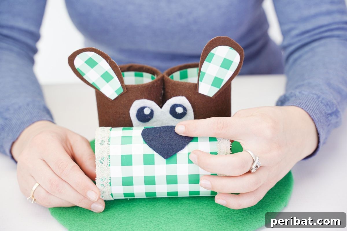 Hand gluing a black felt nose piece onto the top of the green and white checked bottle, forming the dog's snout.