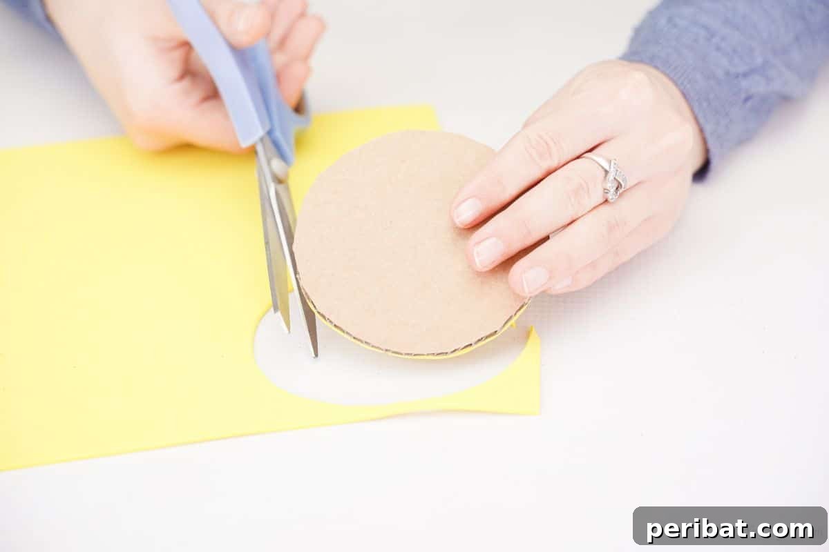 A person trimming excess yellow foam paper from around a cardboard circle with scissors.