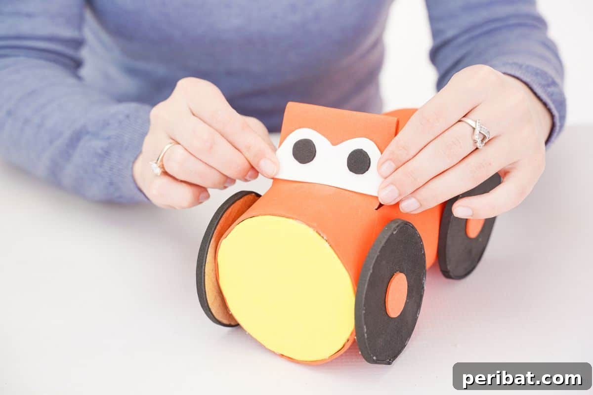 A hand holding a white foam piece with two black circles (eyes) against the orange flap on the car pencil holder.