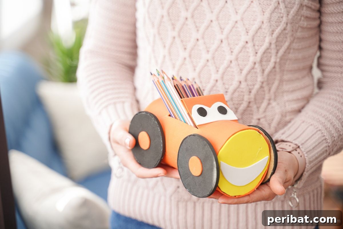 A person holding the finished car pencil holder, showing its yellow front with a white half-moon mouth.