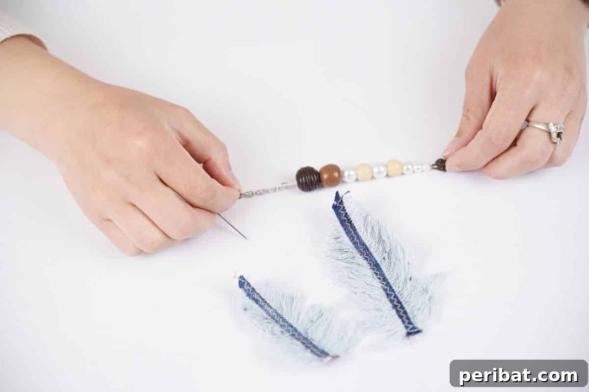 Handmade Denim Feather Keychain 6 a thread of wood beads being held above feather denim pieces