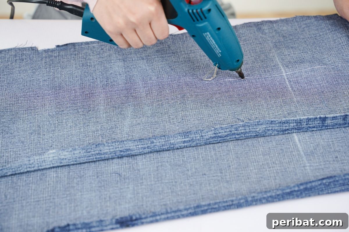 Autumn's Embrace Denim and Burlap Door Wreath 5 Close-up of hot glue being applied to a folded strip of denim fabric.