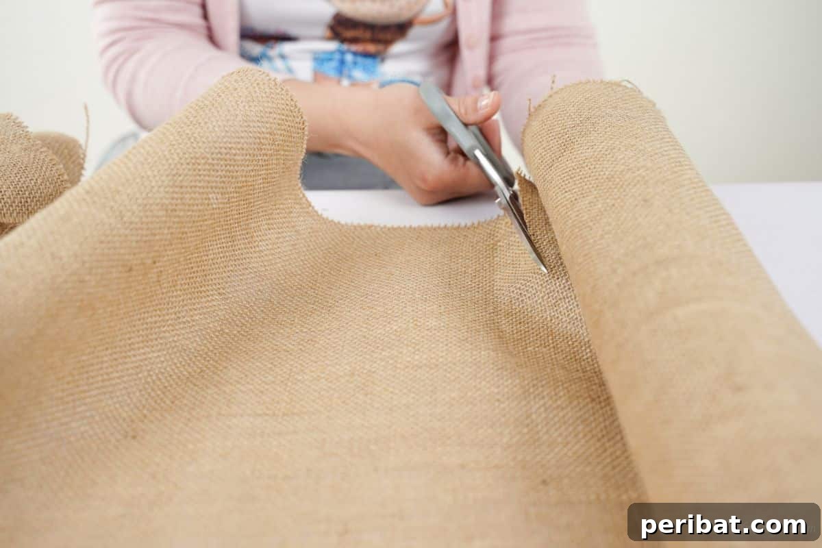 Autumn's Embrace Denim and Burlap Door Wreath 7 A person cutting a strip of burlap fabric with scissors.