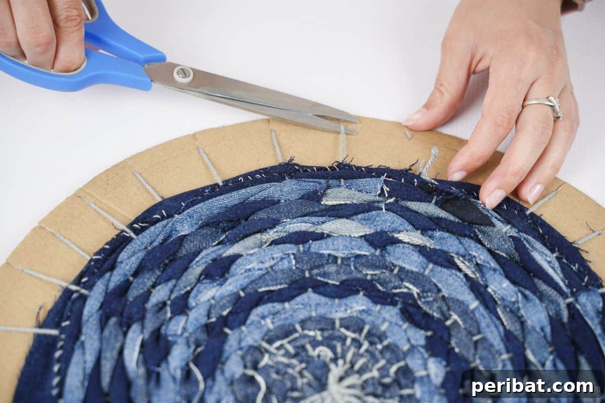 Close-up of denim strips being carefully woven over and under the yarn on the cardboard loom, showing the intricate process.