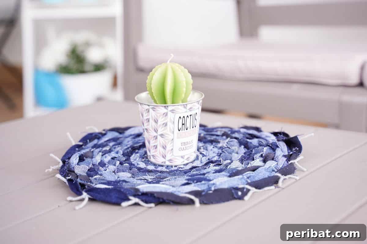 A denim placemat nearing completion, showing the circular woven pattern and the cardboard loom underneath, with some yarn visible.