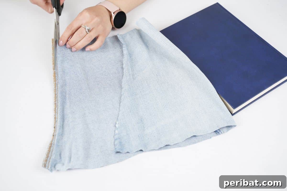 Craft a Stylish Denim Book Cover with Pockets 9 Sharp scissors cutting along the seam of a light denim pant leg to open it flat.
