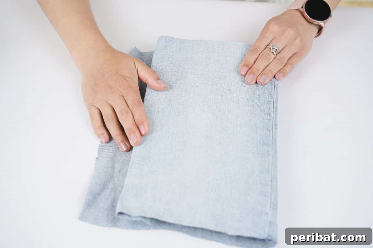Craft a Stylish Denim Book Cover with Pockets 10 A hand smoothly folding a denim flap around the edge of a book cover, preparing it for gluing.