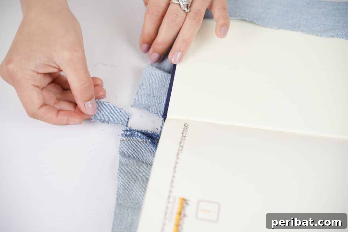 Craft a Stylish Denim Book Cover with Pockets 11 A hand holding and trimming a strip of denim fabric at the top edge of a book's spine area.