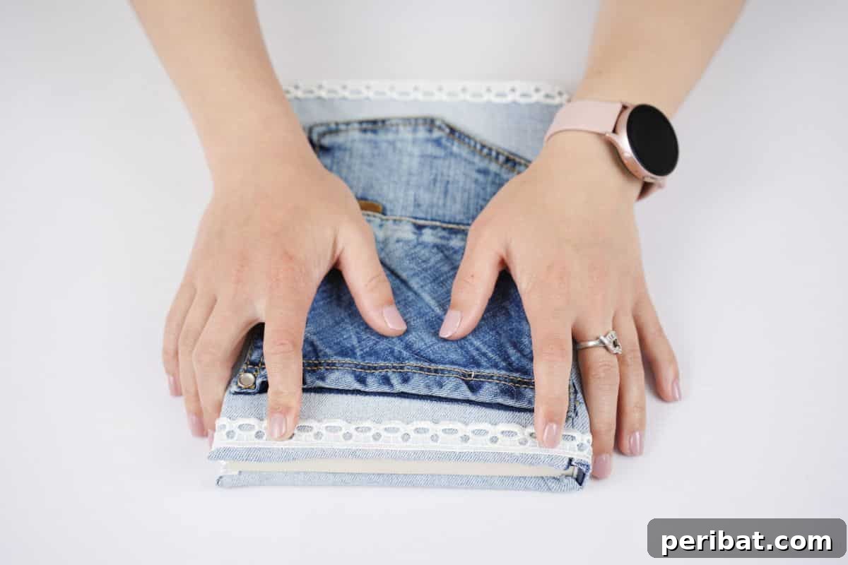Craft a Stylish Denim Book Cover with Pockets 13 Hands carefully holding a piece of lace ribbon onto the top edge of the newly attached denim pocket on a book cover.