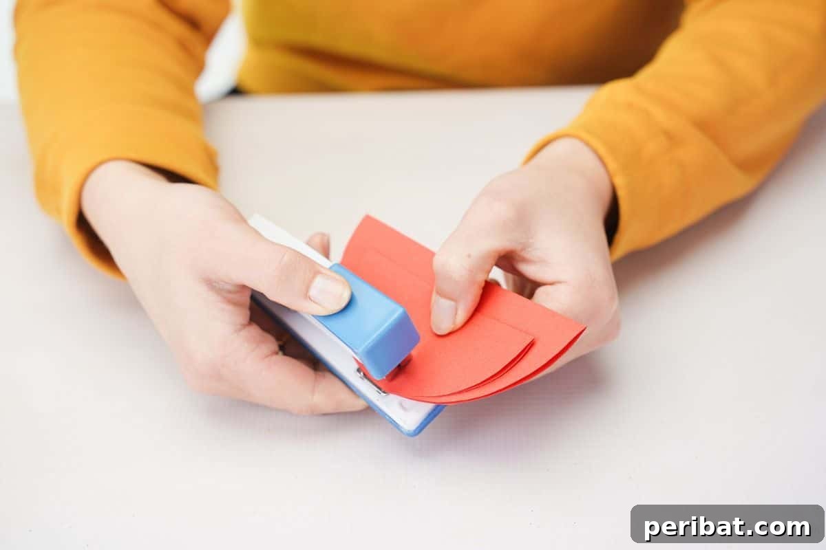 A blue and white stapler stapling two red paper half-circles together at the center.