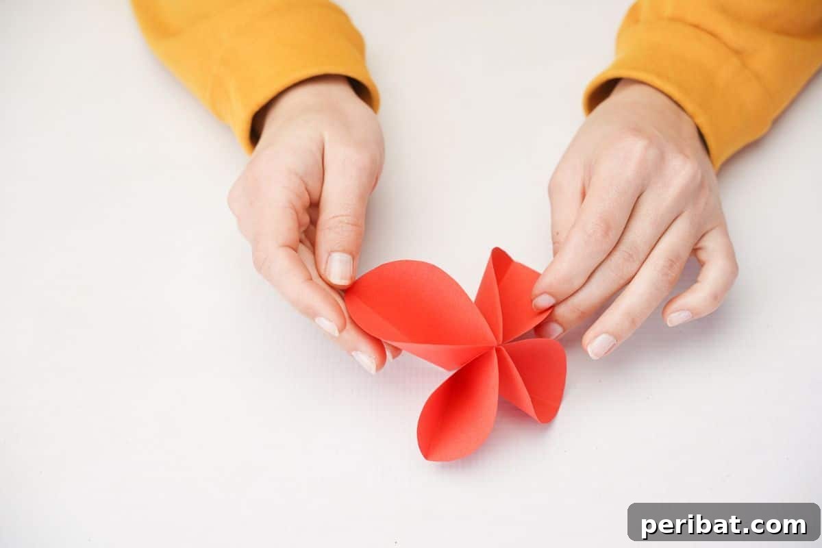 A partially folded red paper butterfly with wings beginning to take shape on a white table.
