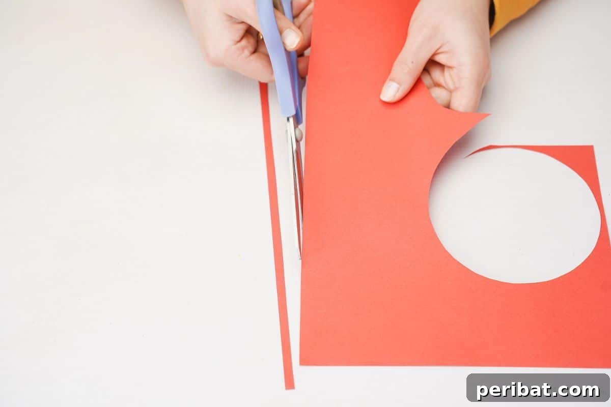 A person cutting a thin strip of red paper with blue scissors for the butterfly's antennae.