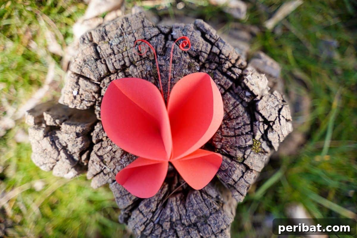A finished red paper butterfly resting on a tree stump, showing its curled antennae.