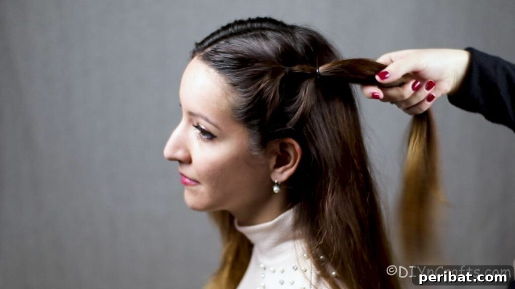 Effortless Festival Bubble Braids 2 Hand holding a side bubble braid against the head, showing the second section tied, incorporating the ends of the first segment.