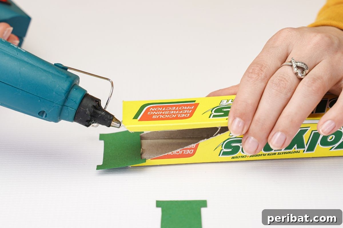 Transform Boxes into Race Cars: Kids Craft Fun 5 Blue hot glue gun applying glue to the end of a cardboard box for the race car nose