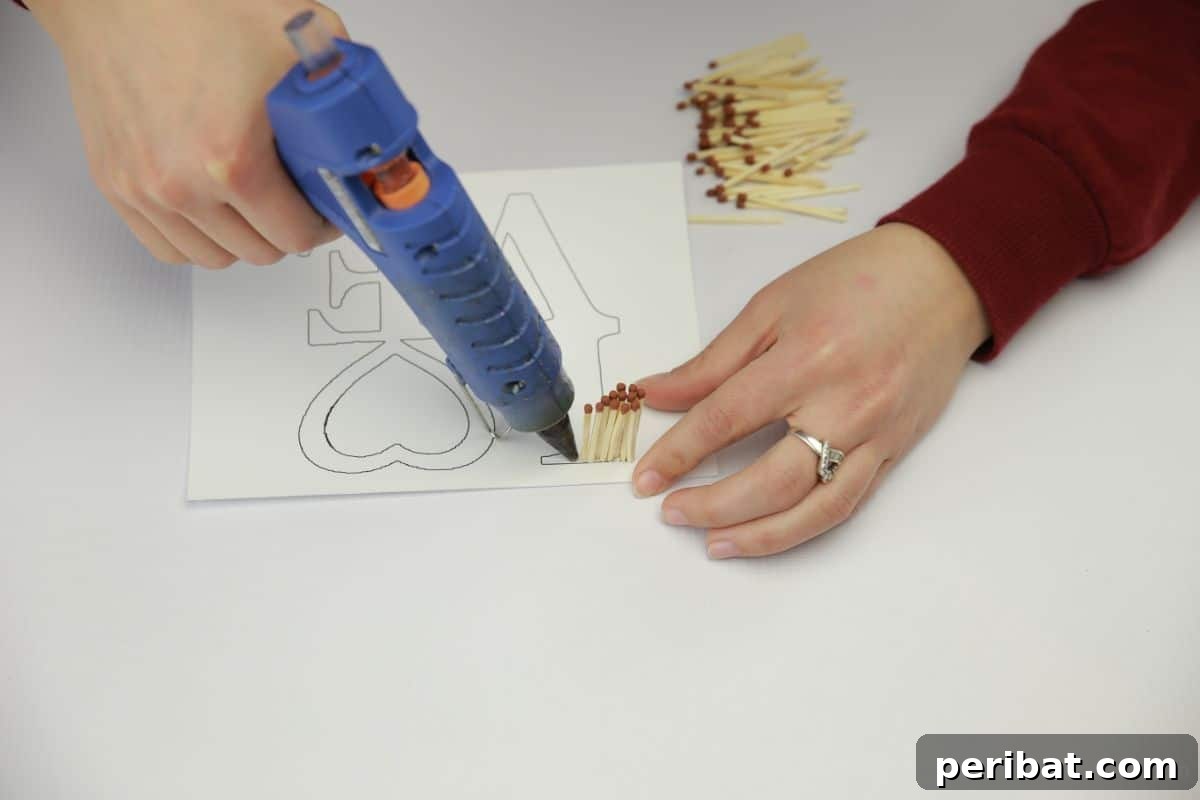 Matchstick Heart Art 4 A hot glue gun is used to carefully attach matchsticks along the traced outline of the word 'LOVE' on paper.