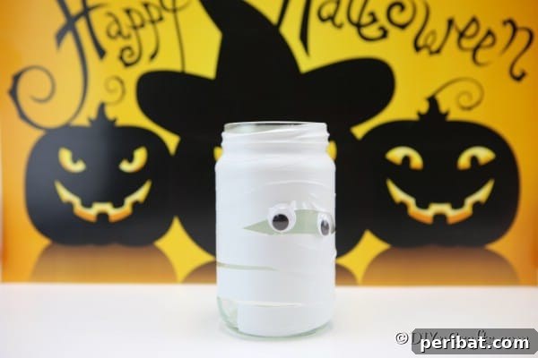 Mason jar lights shaped like mummies sitting on a white counter with a yellow Halloween banner in the background, casting a warm glow.