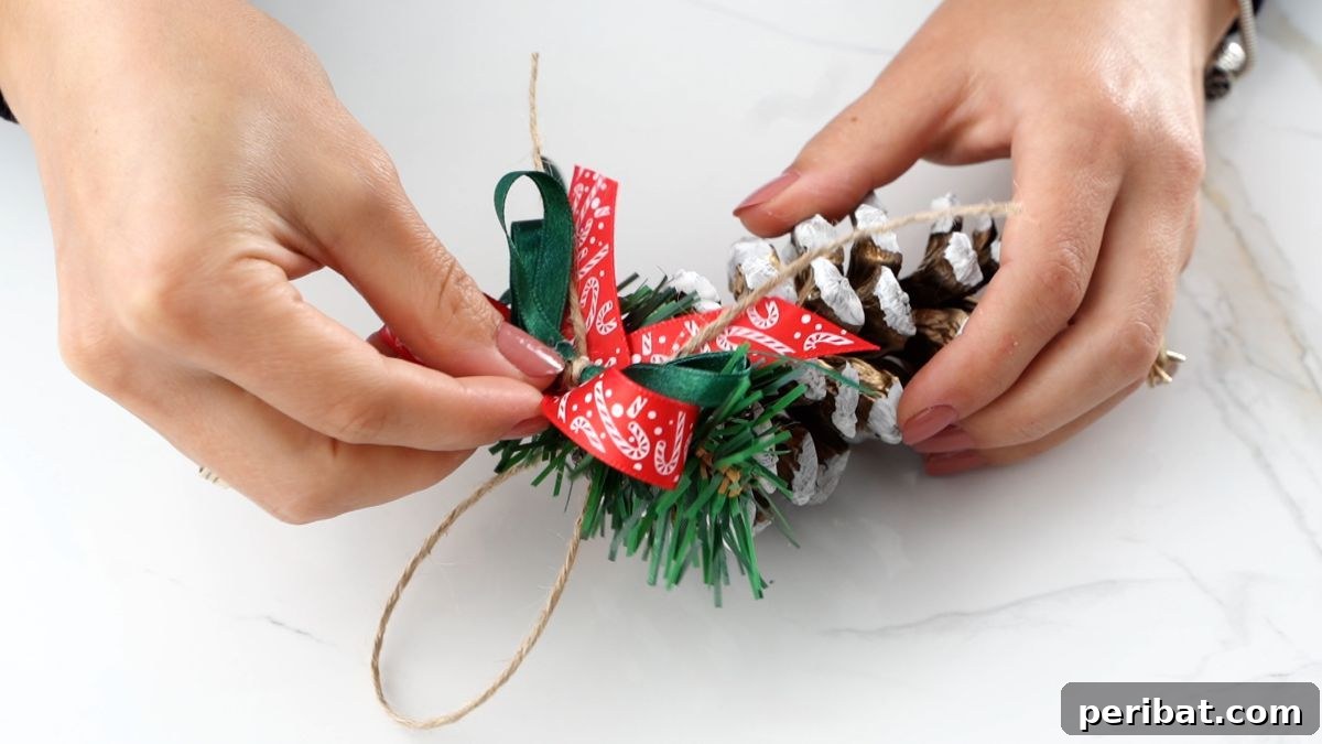DIY Pinecone Christmas Ornaments 11 Carefully gluing a decorative bow onto the top of a finished pinecone ornament, next to the twine hanger