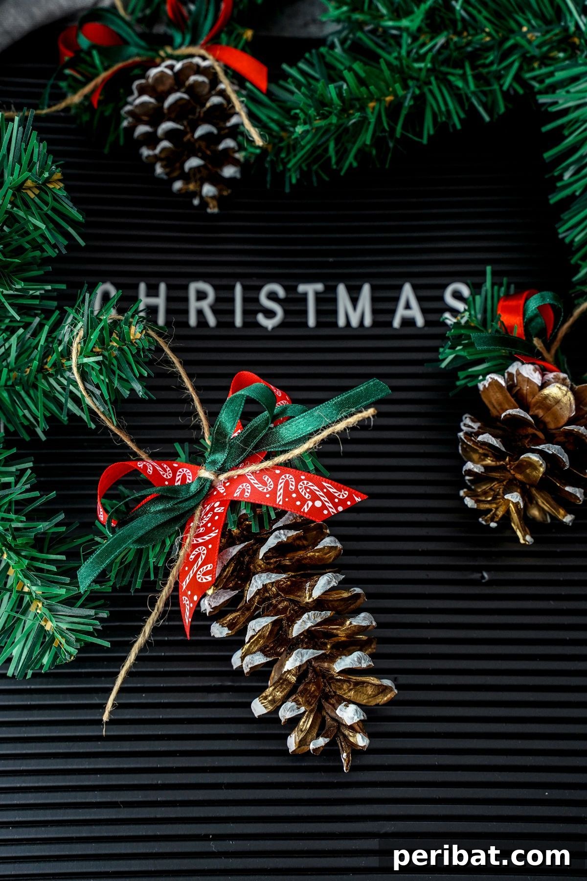 DIY Pinecone Christmas Ornaments 13 A festive pinecone ornament with frosted white tips and a red ribbon, resting on a black board with white Christmas lettering