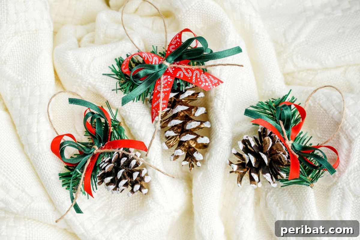 DIY Pinecone Christmas Ornaments 3 Three golden pinecone ornaments with white frosted tips and red ribbons, displayed on a soft white blanket