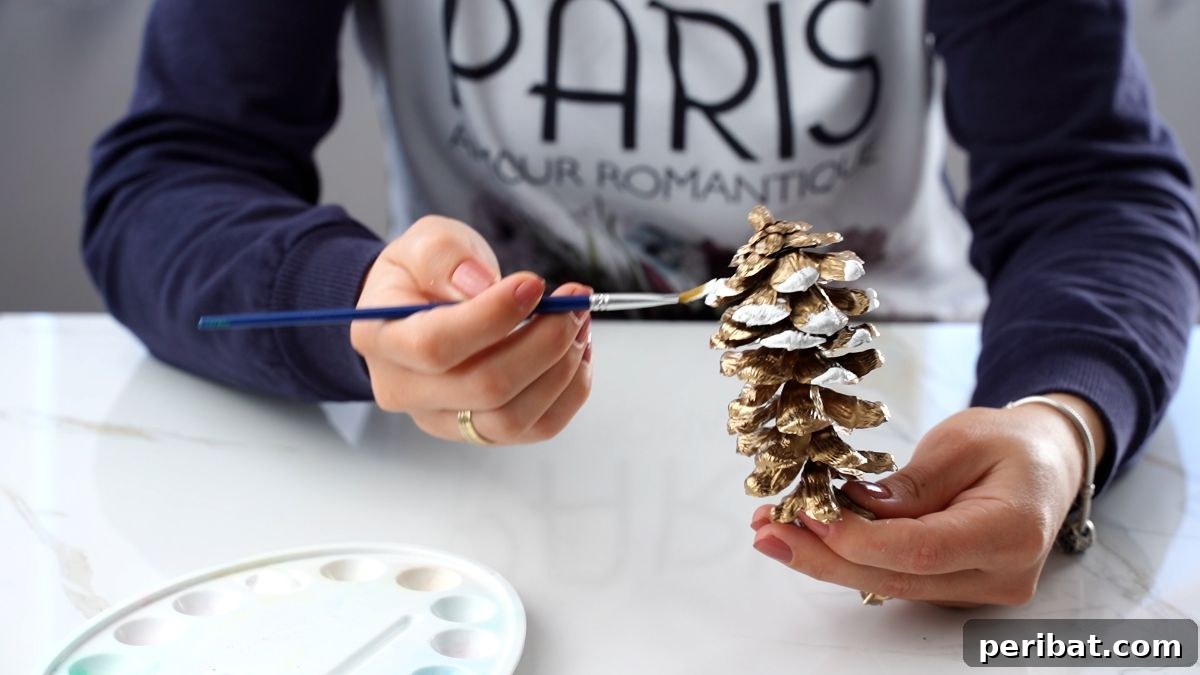 DIY Pinecone Christmas Ornaments 7 A pinecone with white paint applied to the edges of its scales, resembling fresh snow, placed on a white surface