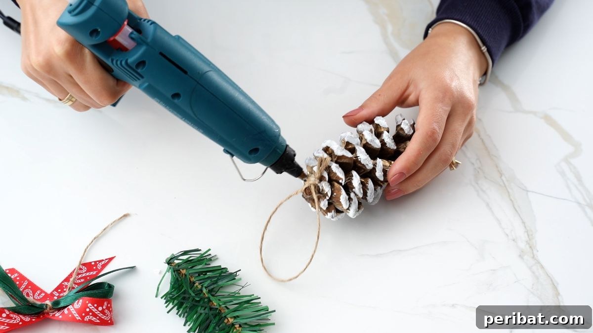 DIY Pinecone Christmas Ornaments 10 Applying hot glue to the top of a pinecone to secure the twine hanger