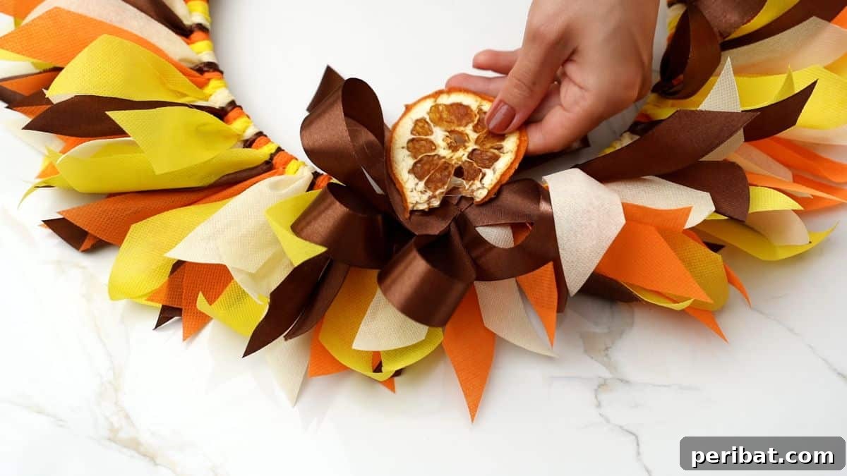 Autumn Farmhouse Wreath from Upcycled Fabric Scraps 12 Hands carefully adding a dried orange slice to the decorative bow of a fall rag wreath.