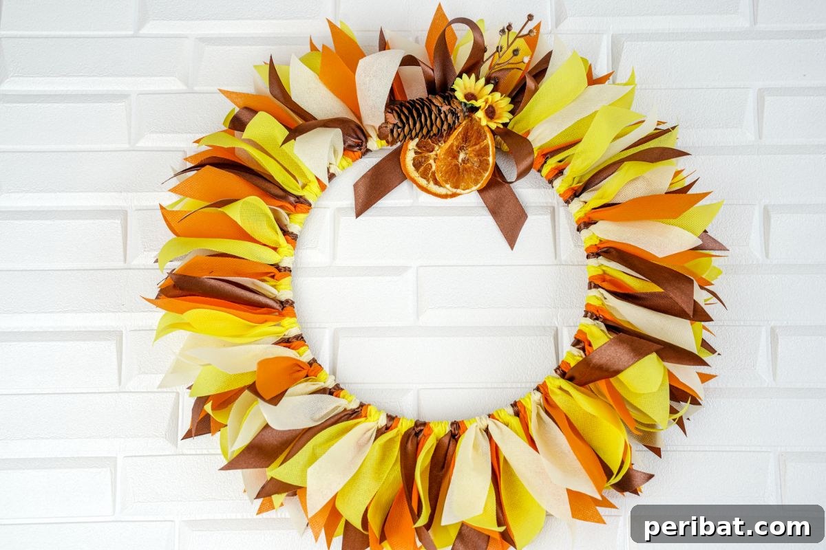 Autumn Farmhouse Wreath from Upcycled Fabric Scraps 16 A vibrant fall rag wreath displayed against a clean white brick background, highlighting its rustic beauty.